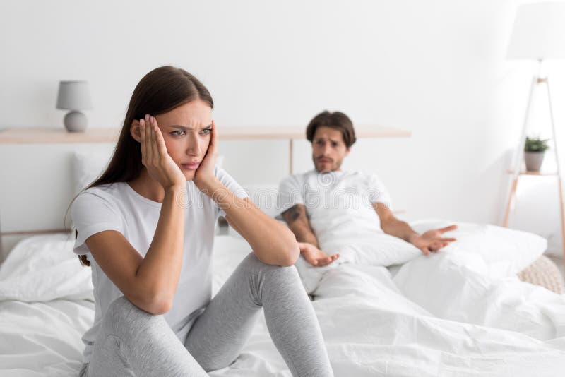 Triste y descontento esposo milenario caucásico con testarudos sentados en la cama gritando a su ofendida esposa