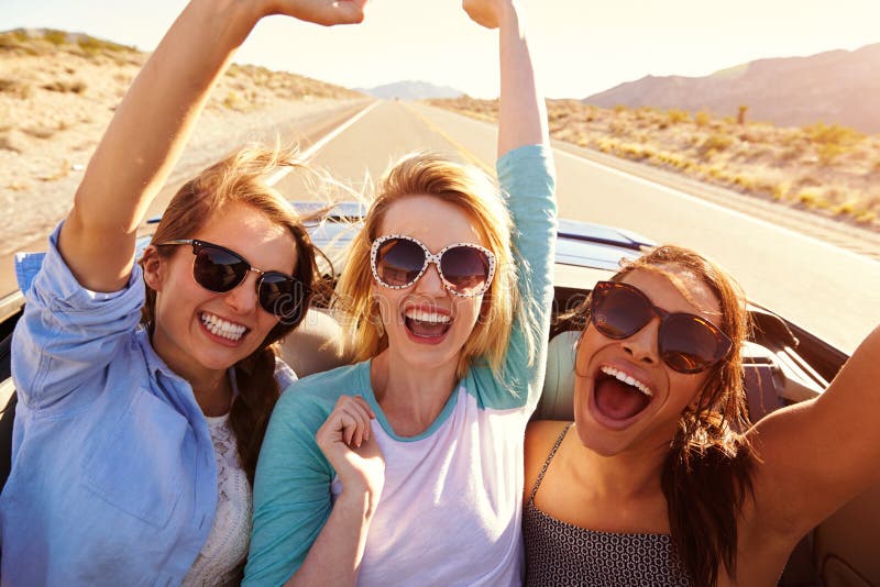 Trois amis féminins sur le voyage par la route derrière la voiture convertible photos stock Trois amis féminins sur le voyage par la route derrière la voiture convertible photos stock