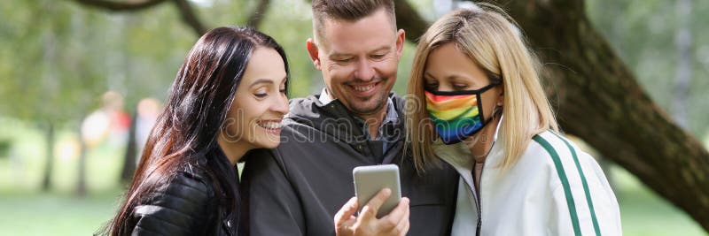 Trois amis heureux regardent l'écran du smartphone une femme porte le masque des couleurs de l'arc-en-ciel. photos libres de droits