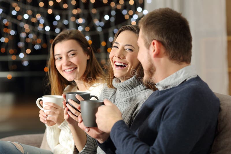 Three friends talking and laughing in the night sitting on a couch in the living room at home. Three friends talking and laughing in the night sitting on a couch in the living room at home