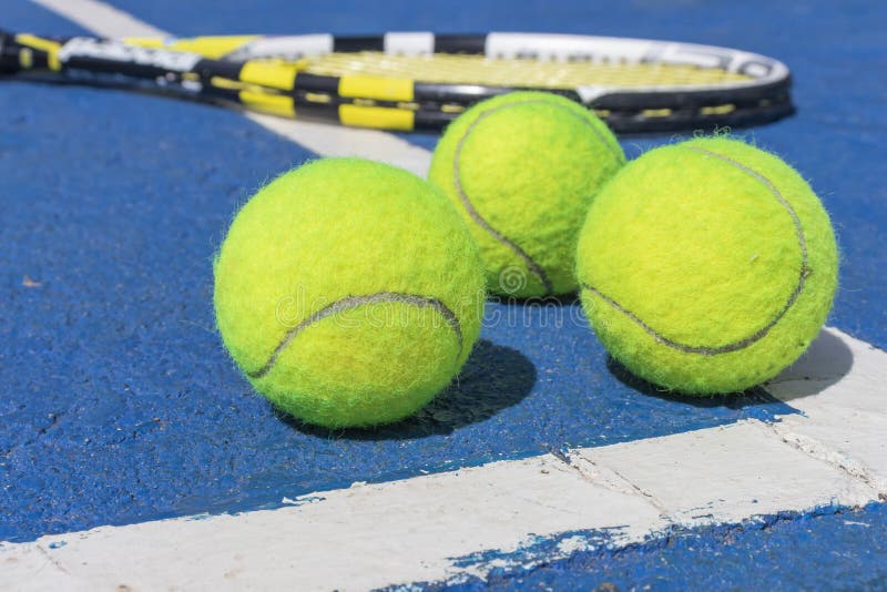 Trois balles de tennis et un mensonge de raquette sur la cour dure photos libres de droits Trois balles de tennis et un mensonge de raquette sur la cour dure photos libres de droits
