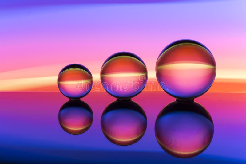 Trois boules de cristal en verre dans une rangée avec un arc-en-ciel de la peinture légère colorée derrière eux images libres de droits Trois boules de cristal en verre dans une rangée avec un arc-en-ciel de la peinture légère colorée derrière eux images libres de droits