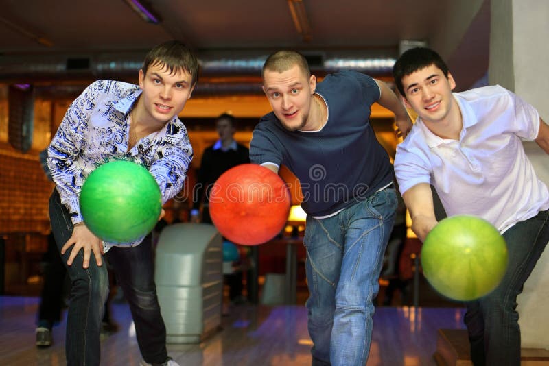 Trois camarades projettent des billes sur la voie dans le club de bowling image libre de droits Trois camarades projettent des billes sur la voie dans le club de bowling image libre de droits