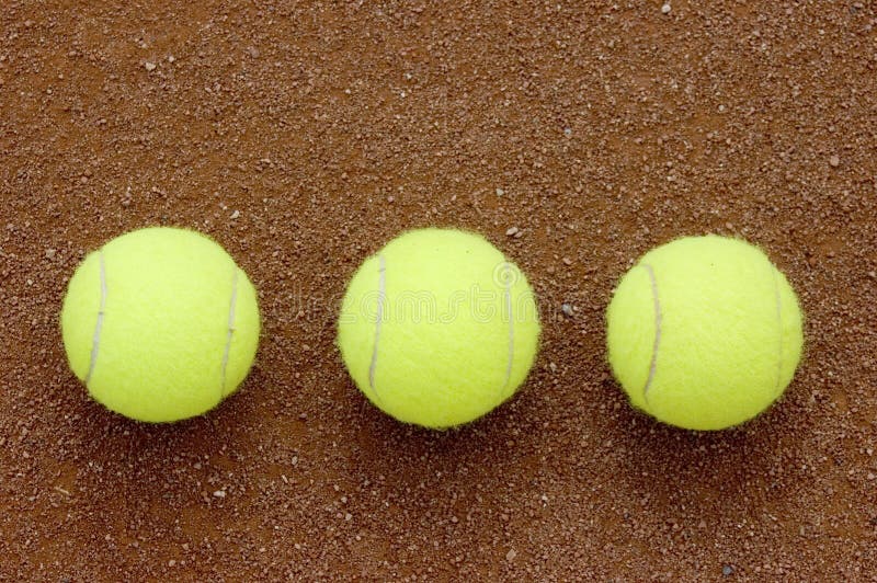 Three tennis balls sitting in the red sand. Three tennis balls sitting in the red sand