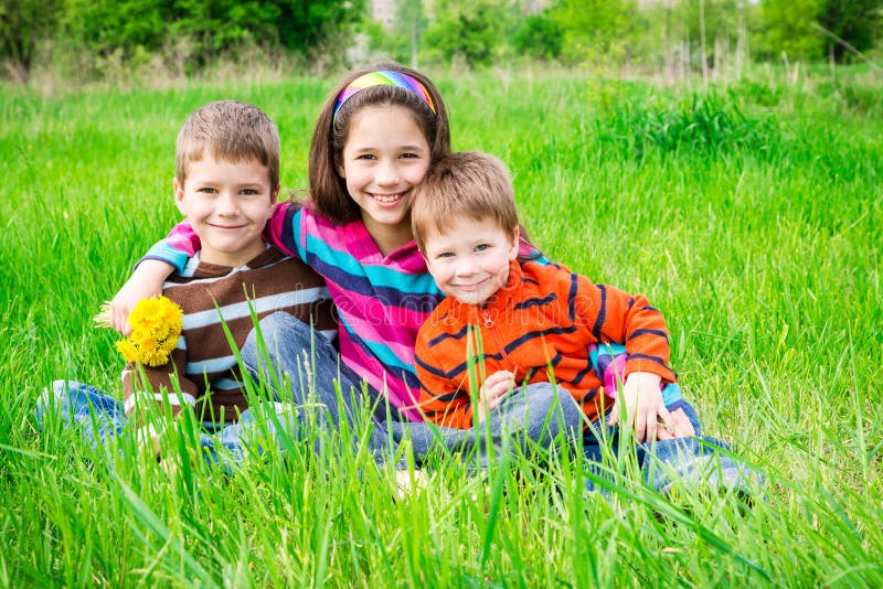 Trois enfants de sourire sur le pré vert photos stock Trois enfants de sourire sur le pré vert photos stock