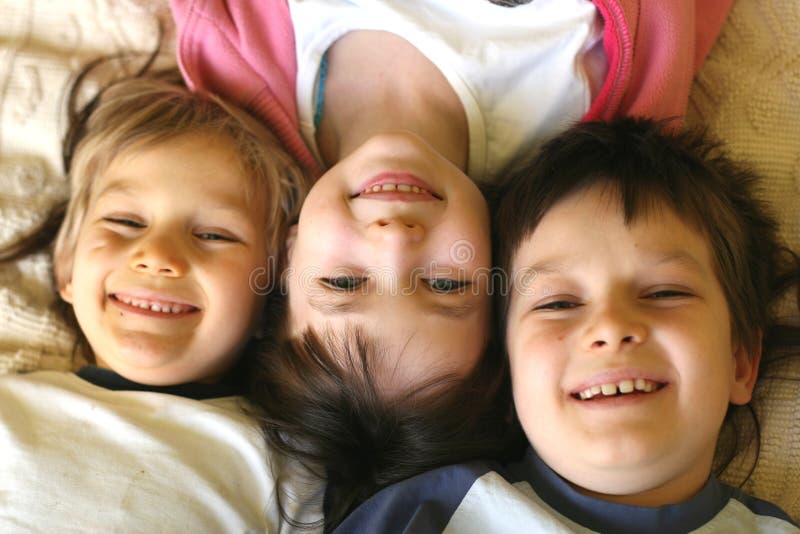 Three children in a playful mood, laying side by side, their heads together. The girl in the middle is laying in the opposite direction. Three children in a playful mood, laying side by side, their heads together. The girl in the middle is laying in the opposite direction.