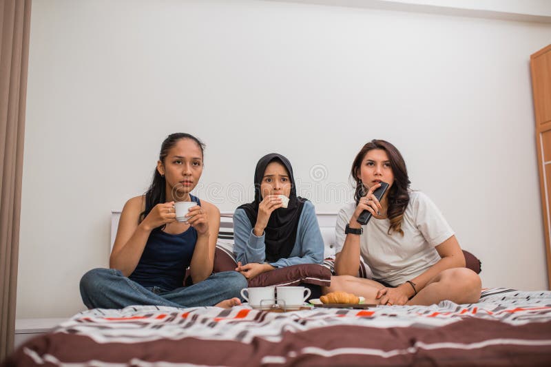 three women with tense faces watching a movie and eating on the bed in the bedroom. three women with tense faces watching a movie and eating on the bed in the bedroom