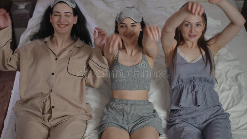 Trois filles avec des masques de sommeil sur la tête regardent la caméra pendant qu'elles sont assis sur un lit dans la chambre. l