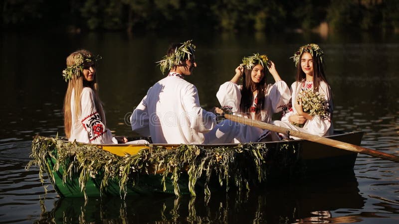 Trois filles et un type dans la robe nationale slave flottant dans un bateau Filles en guirlandes dans un bateau Tradition nation banque de vidéos