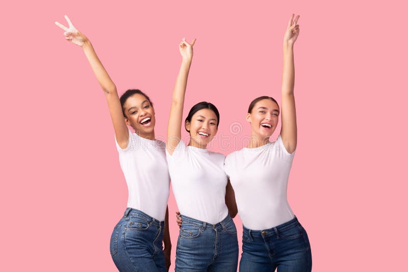 Trois filles heureuses faisant des gestes le V-signe s'amusant sur le fond rose