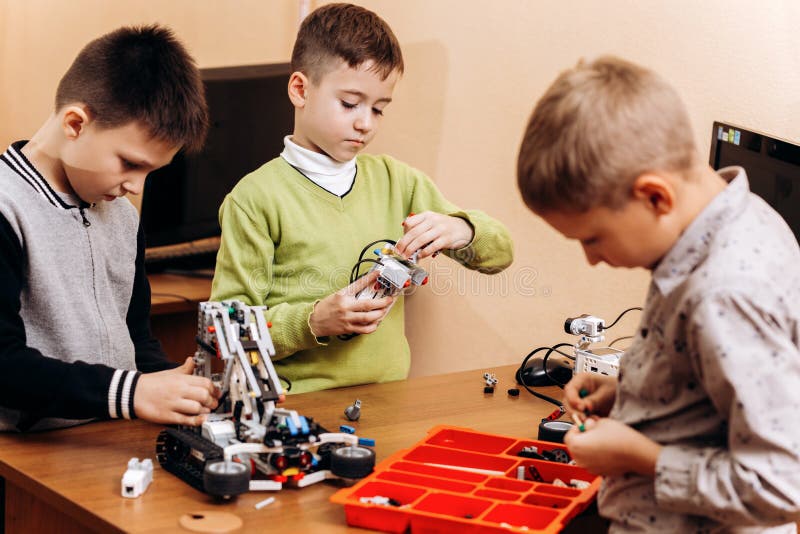 Trois garçons futés font des robots à partir du constructeur robotique au bureau avec l'ordinateur dans l'école de la robotique photo libre de droits Trois garçons futés font des robots à partir du constructeur robotique au bureau avec l'ordinateur dans l'école de la robotique photo libre de droits