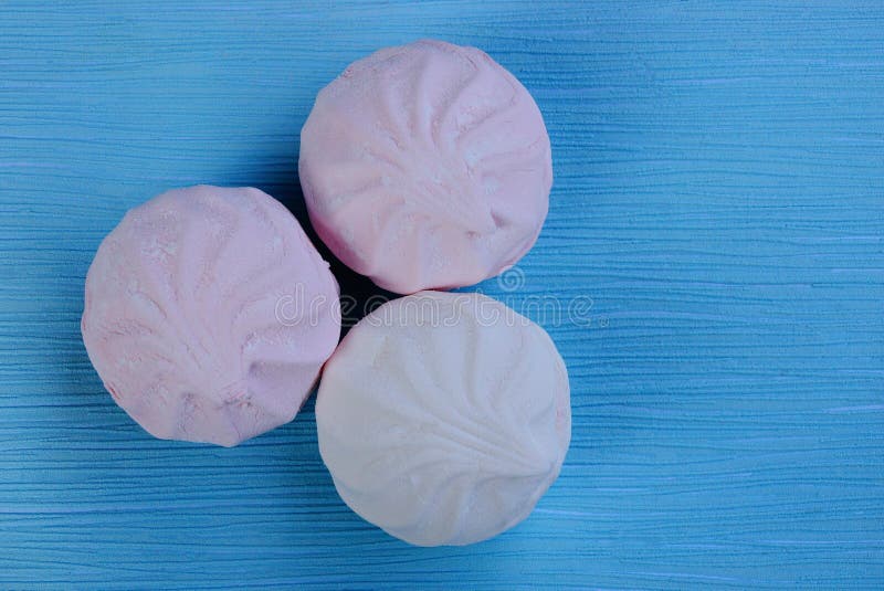 Trois guimauves roses blanches rondes sur une table bleue photographie stock Trois guimauves roses blanches rondes sur une table bleue photographie stock