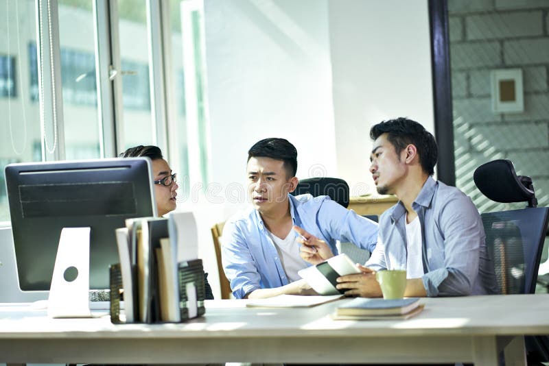 Trois jeunes entrepreneurs asiatiques discutant des affaires dans le bureau photos stock Trois jeunes entrepreneurs asiatiques discutant des affaires dans le bureau photos stock