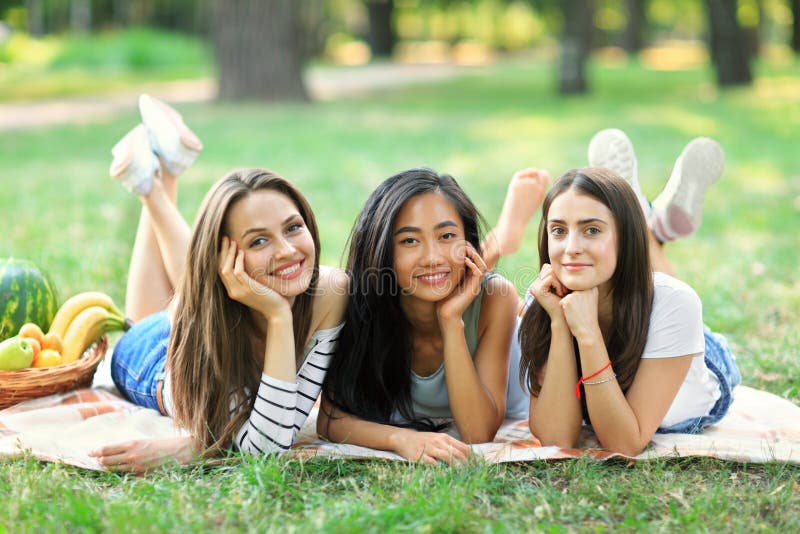 Trois jeunes femmes multiraciales heureuses se trouvant sur l'herbe en parc images libres de droits Trois jeunes femmes multiraciales heureuses se trouvant sur l'herbe en parc images libres de droits