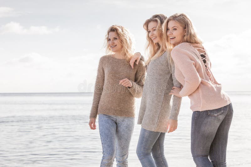 Trois modèles à la mode extérieurs. Trois femmes à la mode utilisant des chandails par le temps automnal chaud passant leur temps gratuit sur la plage ensoleillée Mannequins extérieurs ayant l'amusement