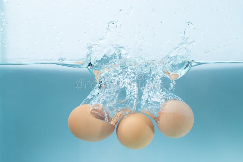 Trois oeufs éclaboussent avec de l'eau sur le bleu photographie stock Trois oeufs éclaboussent avec de l'eau sur le bleu photographie stock