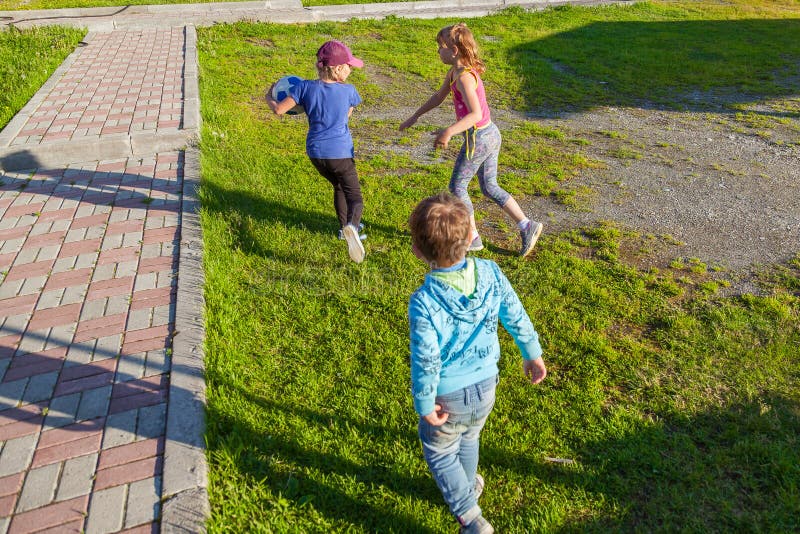 Trois petits enfants, deux filles et une course de garçon sur l'herbe verte dans la cour pendant les jeux, se chassant pour empor photo stock Trois petits enfants, deux filles et une course de garçon sur l'herbe verte dans la cour pendant les jeux, se chassant pour empor photo stock