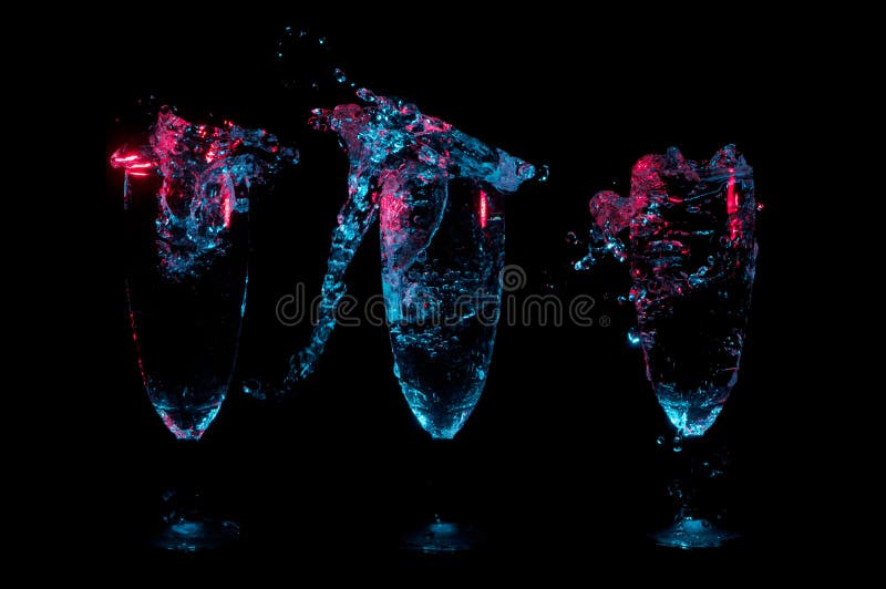 Trois verres de fantaisie dans une rangée avec grand éclabousse sous les lumières rougeoyantes bleues et rouges sur un fond noir images stock Trois verres de fantaisie dans une rangée avec grand éclabousse sous les lumières rougeoyantes bleues et rouges sur un fond noir images stock