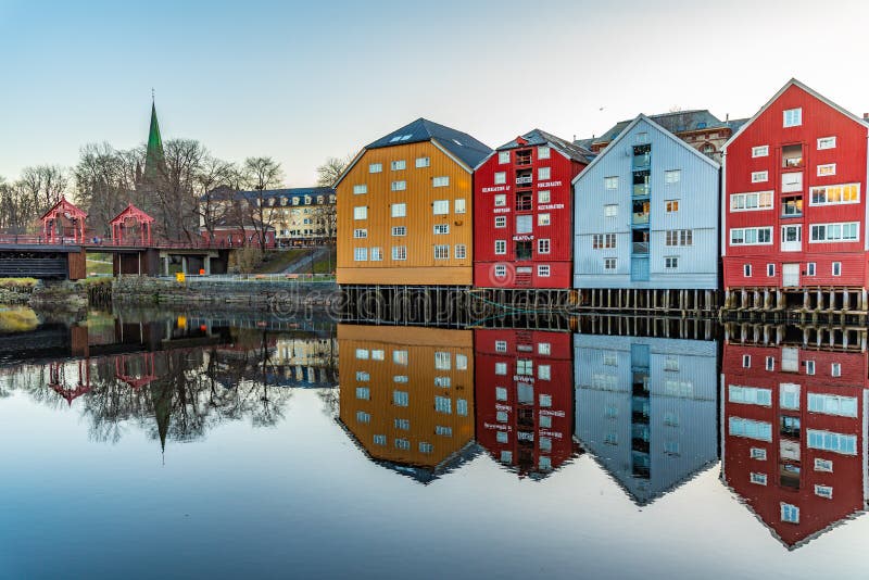 TRONDHEIM, NORWAY, APRIL 17, 2019: Sunset view of Nidaros cathedral and colorful timber houses surrounding river Nidelva in the Brygge district of Trondheim, Norway. TRONDHEIM, NORWAY, APRIL 17, 2019: Sunset view of Nidaros cathedral and colorful timber houses surrounding river Nidelva in the Brygge district of Trondheim, Norway