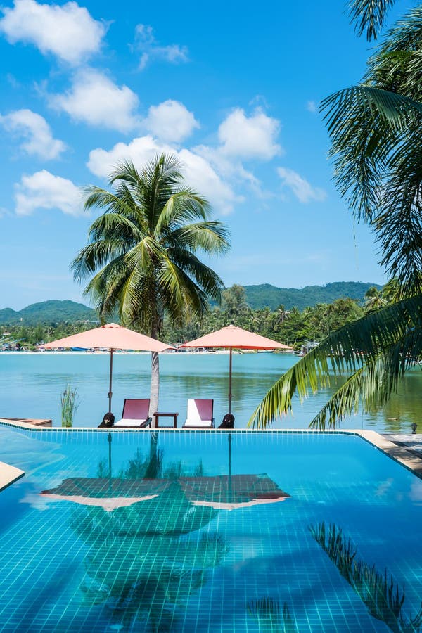 Tropical beach resort with clear water swimming pool with beach umbrellas and chairs near the sea.