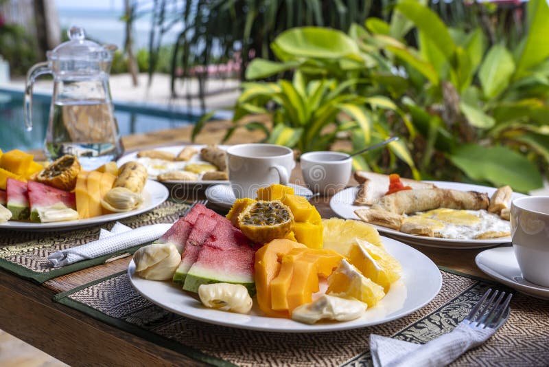 Tropical breakfast of fruit, coffee and scrambled eggs and banana pancake for two on the beach near sea