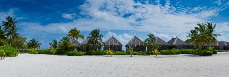 Tropical bungalos panorama view at resort with white sand and palm trees at Maldives