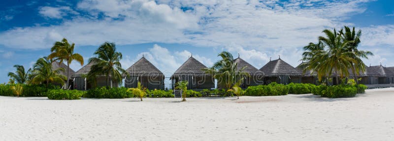 Tropical bungalos panorama view with white sand and palm trees at Maldives