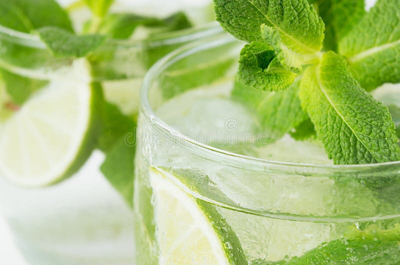 Tropical fresh green cold cocktail closeup with mint, lime, ice, straw, water drops, bubbles, blur.