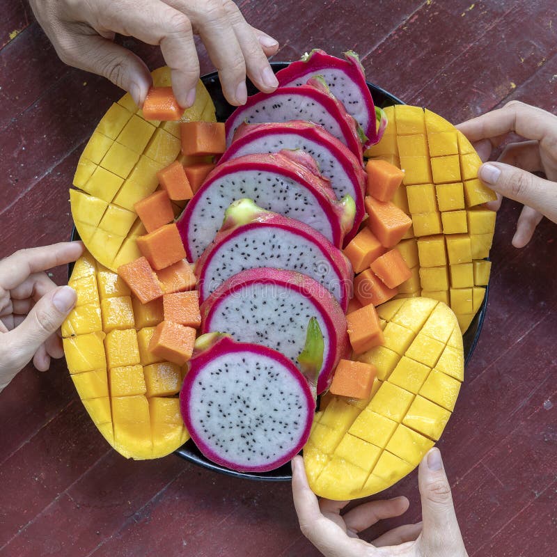 Tropical fruits assortment on a plate and people hands, close up. Yummy dessert, close up. Mango, papaya, pitahaya and hands, top royalty free stock photography Tropical fruits assortment on a plate and people hands, close up. Yummy dessert, close up. Mango, papaya, pitahaya and hands, top royalty free stock photography