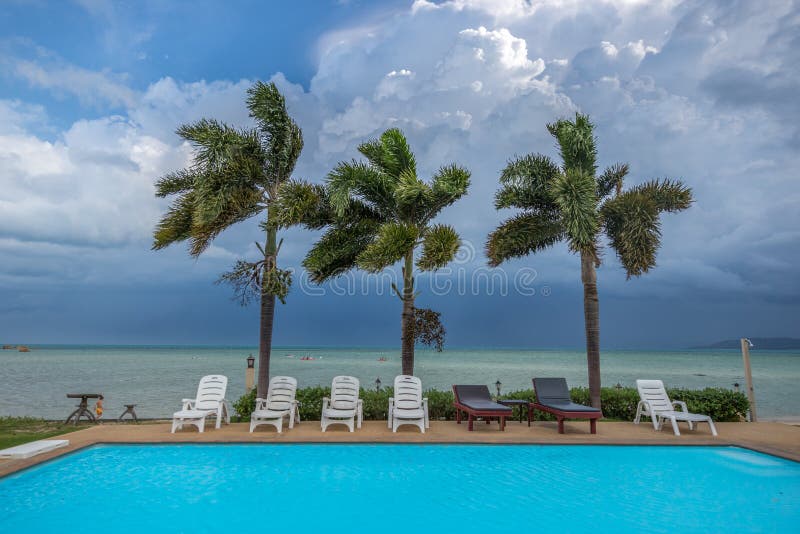 Tropical Resort Pool with Lounge Chairs, Palm Trees, at the Ocean and Clouds sky background view