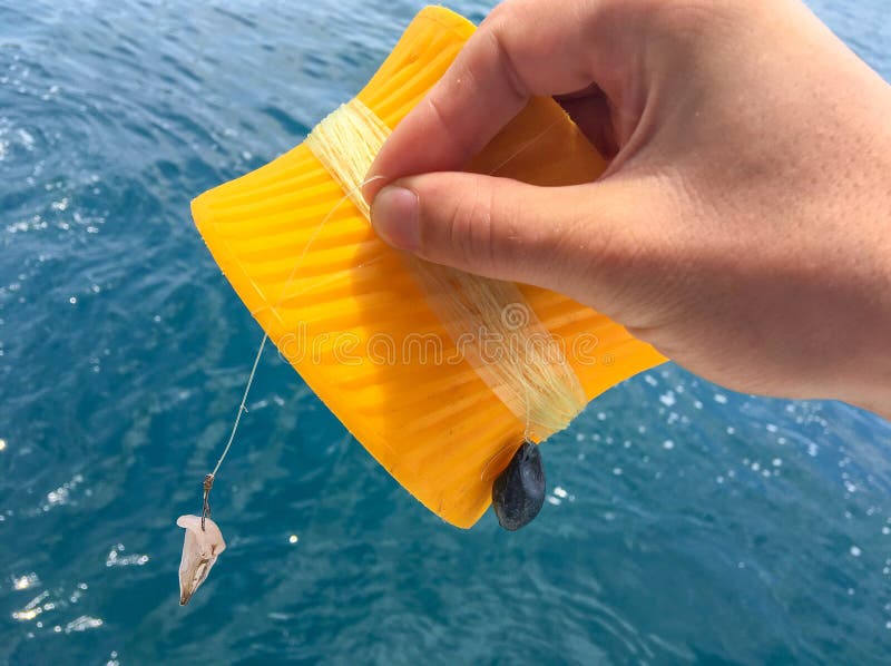 Tropical sea fishing on boat board in Asia. Squid bait on hook. Male hand holds a round plastic fishing rod with fishing line