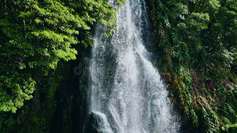 Tropical waterfall cascading down rocky ledges drone shot. Serene lush paradise