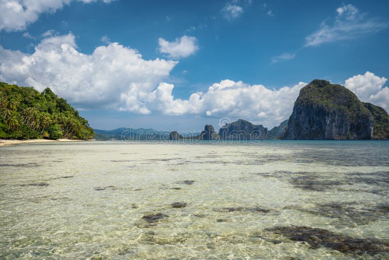 Scenic tropical landscape. Shallow lagoon, sandy beach with palm trees. Exotic islands in background. El Nido, Palawan, Philippines. Scenic tropical landscape. Shallow lagoon, sandy beach with palm trees. Exotic islands in background. El Nido, Palawan, Philippines.