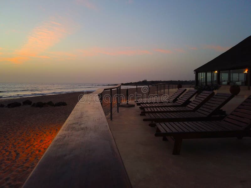 Tropische achtergrond met paar van ligstoelen bij zonsondergang door overzees Het is mooie mening van gouden zon van hotel royalty-vrije stock afbeelding Tropische achtergrond met paar van ligstoelen bij zonsondergang door overzees Het is mooie mening van gouden zon van hotel royalty-vrije stock afbeelding