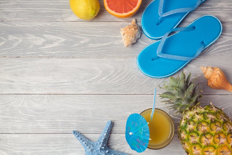 Tropical summer vacation background with pineapple, juice and flip flops on wooden table. View from above. Flat lay. Tropical summer vacation background with pineapple, juice and flip flops on wooden table. View from above. Flat lay