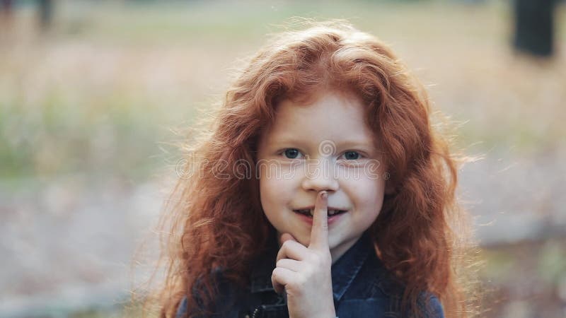 Troszkę śliczna rudzielec dziewczyny pozycja w jesień parku patrzeje w kamerę i pokazuje gest naciska jego Shhh