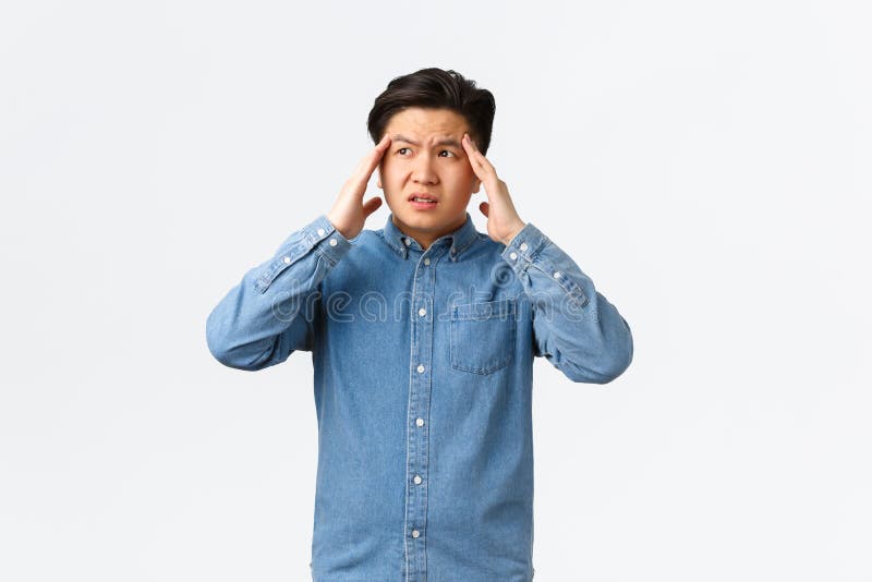 Troubled and uneasy asian man looking perplexed, having complicated situation. Guy with headache touching head and looking away, suffering painful migraine, standing white background.