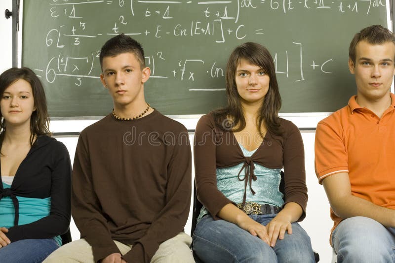 Small group of teenagers sitting in front of blackboard. Two boys and two girls. Looking at camera, front view. Small group of teenagers sitting in front of blackboard. Two boys and two girls. Looking at camera, front view