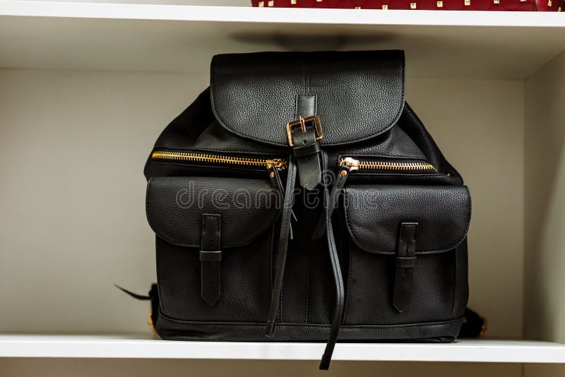 Trouxa de couro preta com os bolsos dourados do z?per em uma prateleira branca na loja imagem de stock Trouxa de couro preta com os bolsos dourados do z?per em uma prateleira branca na loja imagem de stock