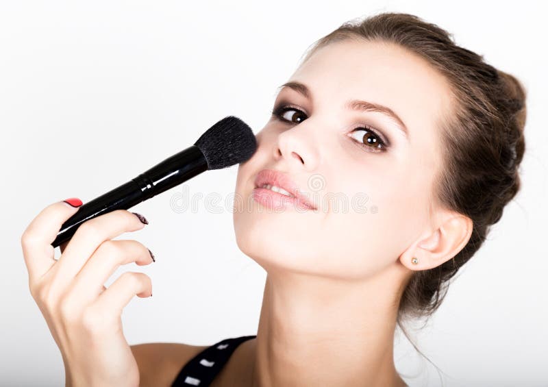 Trucco d'applicazione di modello femminile sul suo fronte Bella giovane donna che applica fondamento sul suo fronte con una spazz fotografie stock Trucco d'applicazione di modello femminile sul suo fronte Bella giovane donna che applica fondamento sul suo fronte con una spazz fotografie stock