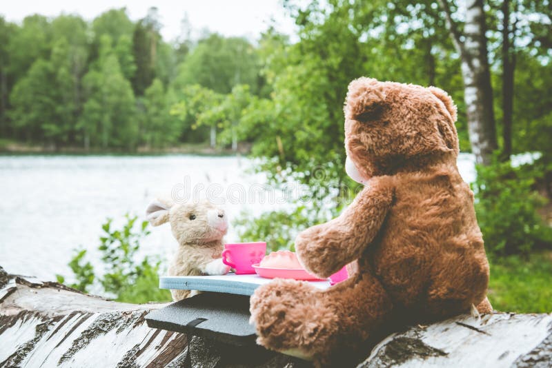 True friends - the rabbit and the little bear are sitting on the grass during a picnic in a park