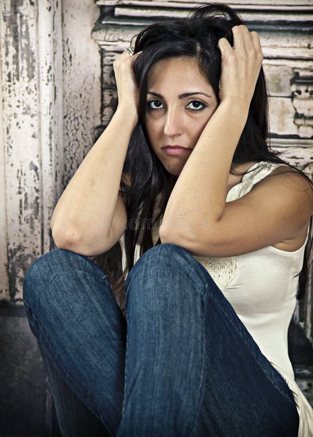 Sad, worried young woman sitting and holding her head in front of an old weathered door. Depression. Sad, worried young woman sitting and holding her head in front of an old weathered door. Depression.