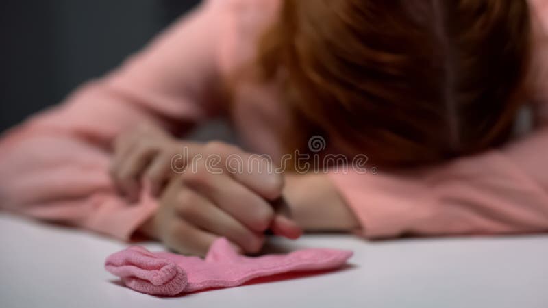 Tryckt ned ung dam som gråter i förtvivlan, rosa barnsocka på tabellen, ofruktbarhet arkivfoton Tryckt ned ung dam som gråter i förtvivlan, rosa barnsocka på tabellen, ofruktbarhet arkivfoton