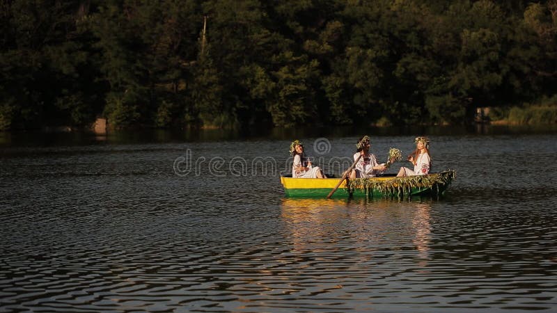 Trzy młodej dziewczyny unosi się na rzece z długie włosy w łodzi Dziewczyny w Slawistycznych kostiumach z wiankiem na jego głowie
