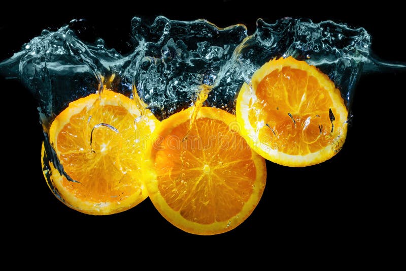 Close-up of three sliced oranges plunged underwater with splashes on black. Close-up of three sliced oranges plunged underwater with splashes on black