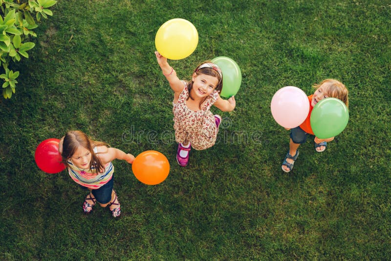 Three happy little kids playing with colorful balloons outdoors, top view. Three happy little kids playing with colorful balloons outdoors, top view