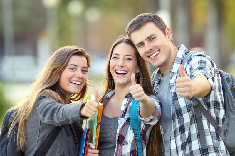 Three happy students looking at you with thumbs up in an university campus. Three happy students looking at you with thumbs up in an university campus