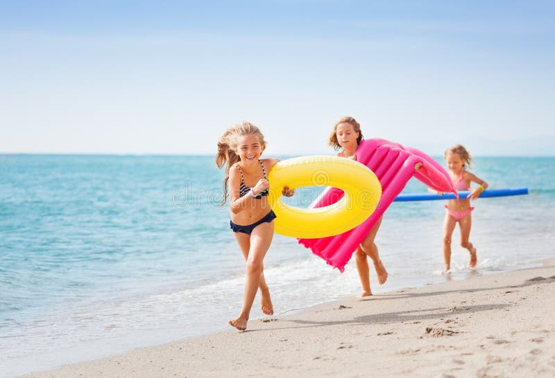 Three happy girls with swimming tools running one after another along the sandy beach. Three happy girls with swimming tools running one after another along the sandy beach