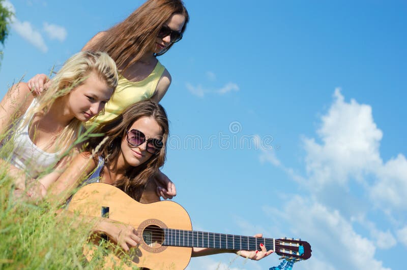 Trzy szczęśliwej pięknej kobiety śpiewa gitarę i bawić się przeciw niebieskiemu niebu obrazy stock Trzy szczęśliwej pięknej kobiety śpiewa gitarę i bawić się przeciw niebieskiemu niebu obrazy stock
