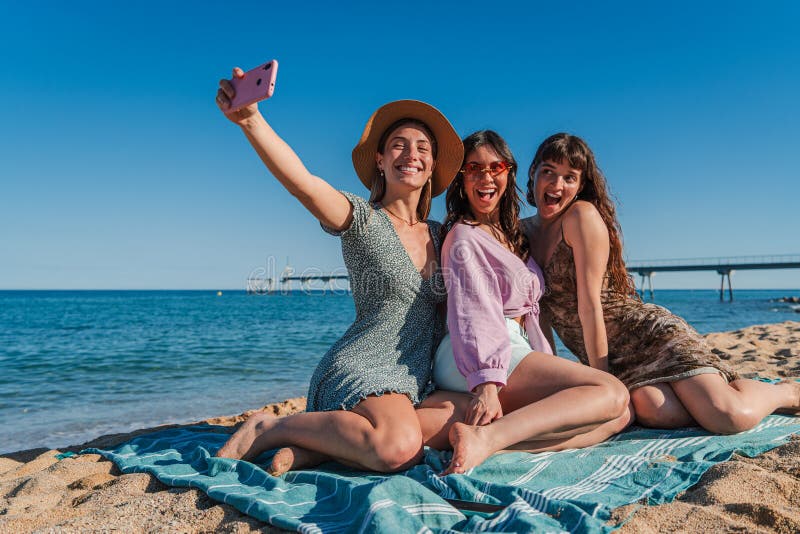Trzy ubrane kobiety leżące na piasku plaży robiące portret selfie z komórką. grupa dziewcząt uśmiechających się i zdjęcie royalty free